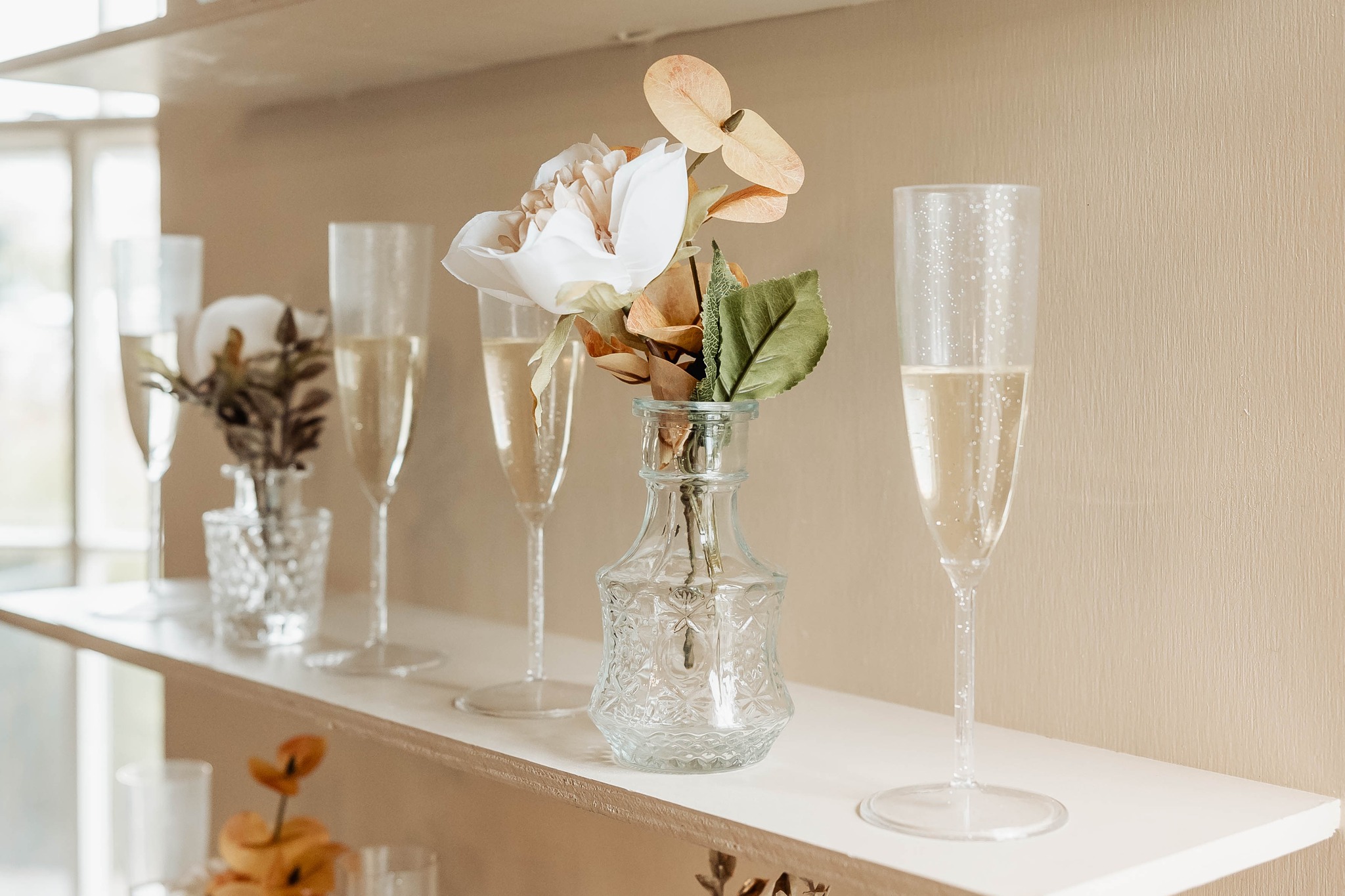 Close up of champagne sitting on a ledge with vases of flowers.