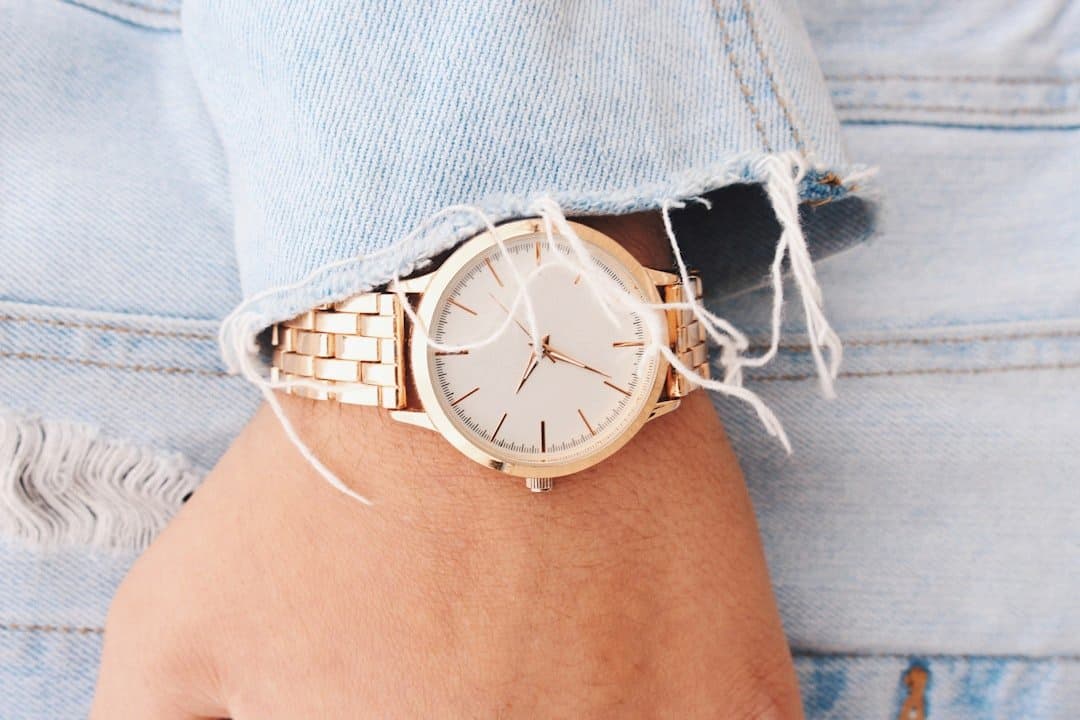 A close up of a Caucasian female's hand with a gold watch slightly covered by the sleeve of her denim jacket.